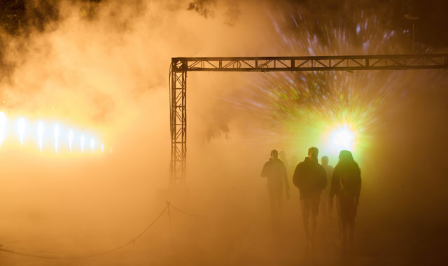 Moody shot as a silhouette of 3 people are seen exiting From the Light Flow: Bena Koorliny through smoke lit in yellow. 