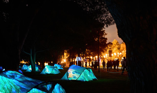 A series of lit-up tents low to the ground with crowds in the background enjoying From the Light Flow: Bena Koorliny.