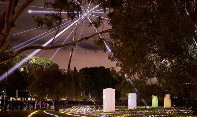 Image of a crane holding a ball projecting lights high in the sky above cylinders of light from From the Light Flow: Bena Koorliny.